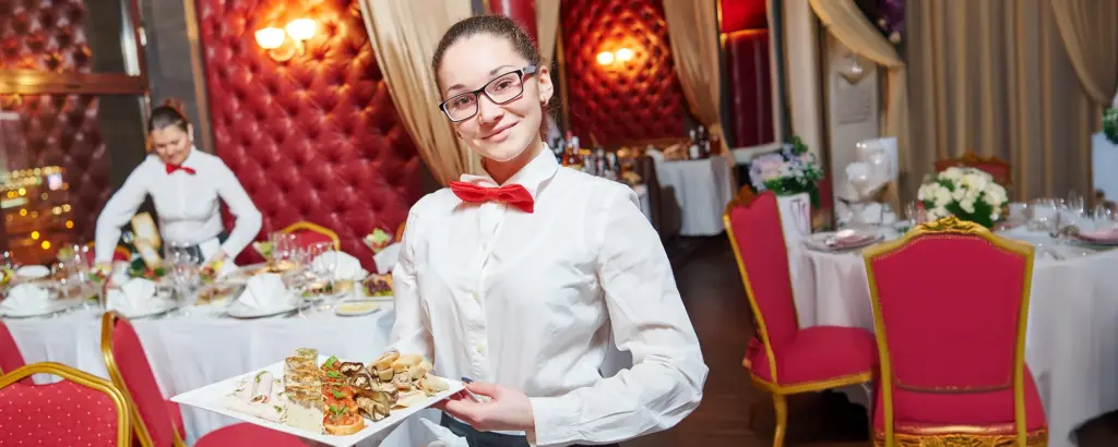Kellnerin in einem eleganten Restaurant serviert ein Tablett mit Vorspeisen, umgeben von reich dekorierten Tischen.