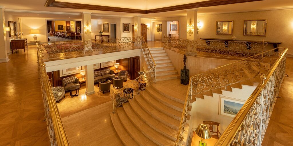Luxuriöse Hotel-Lobby mit gewundener Marmortreppe, goldenen Geländern, eleganten Sitzbereichen und warmem Ambiente
