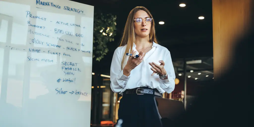 Frau präsentiert Marketingstrategie an Tafel in modernem Büro.
