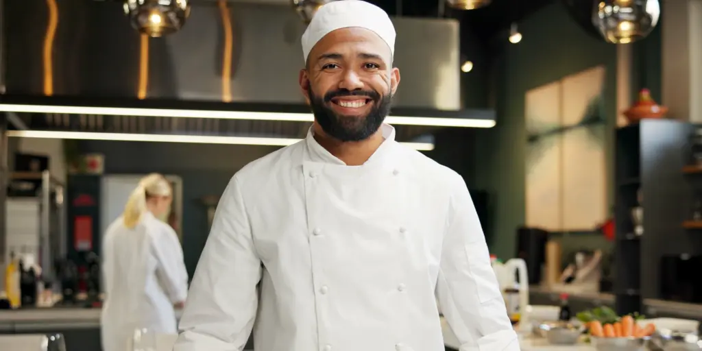 Ein lächelnder Koch in Weiß vor moderner Kücheneinrichtung.