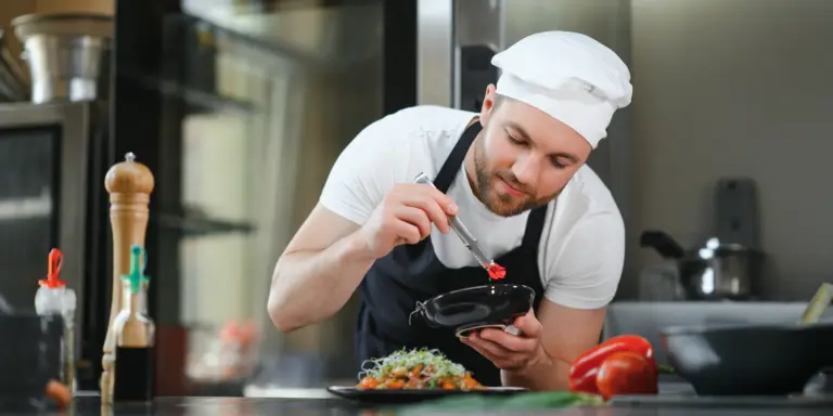 Ein Koch verfeinert ein Gericht mit Präzision in einer modernen Küche, umgeben von frischen Zutaten.