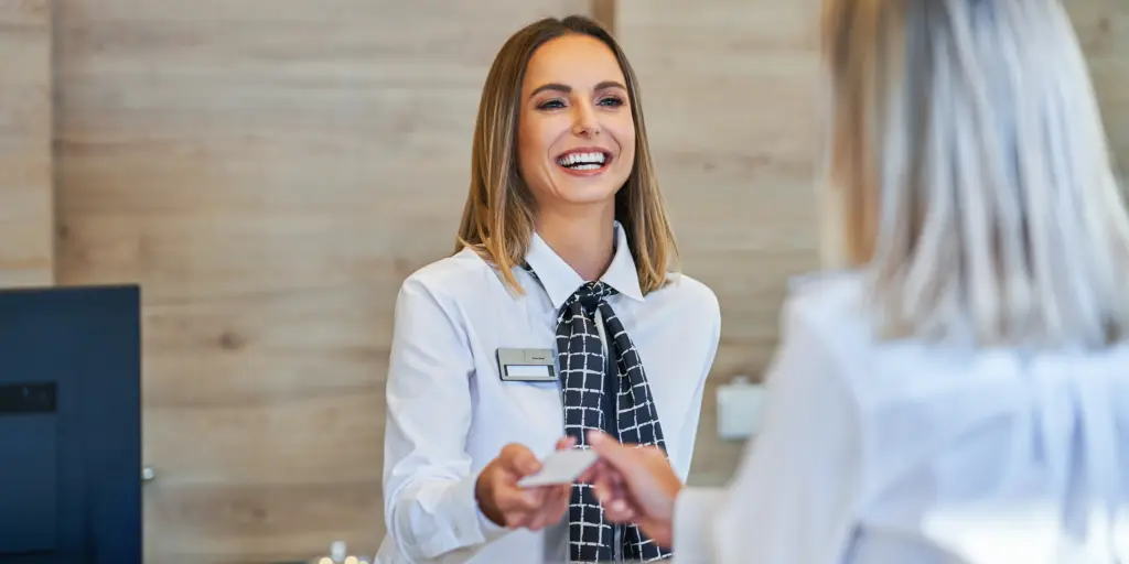 Freundlicher Empfang, lächelnde Rezeptionistin übergibt Karte an Gast im modernen Hotel.