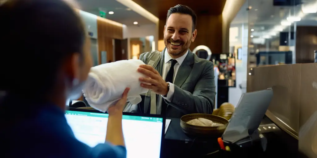 Mann in Business-Anzug lächelt, erhält Handtuch an Rezeption, freundliche Hotel- oder Büroatmosphäre.