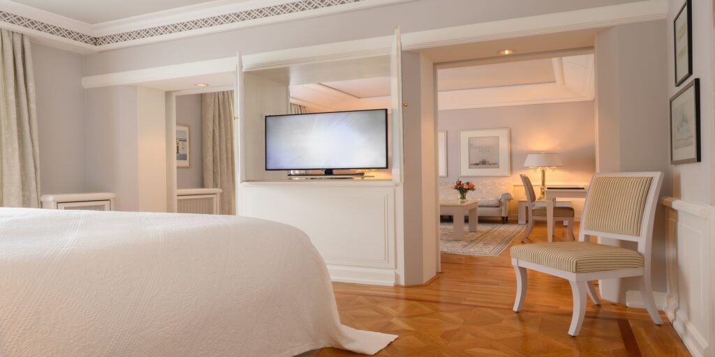 Helle, elegante Hotelsuite mit Kingsize-Bett, TV, separatem Wohnbereich und klassischer Einrichtung
