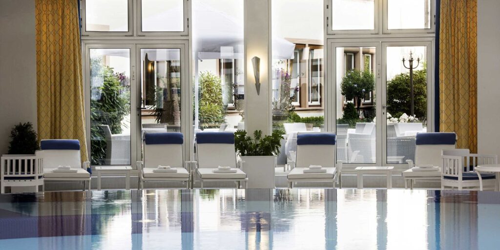 Hotel-Innenpool: Liegen, Panoramafenster und Gartenblick im stilvollen Wellnessbereich
