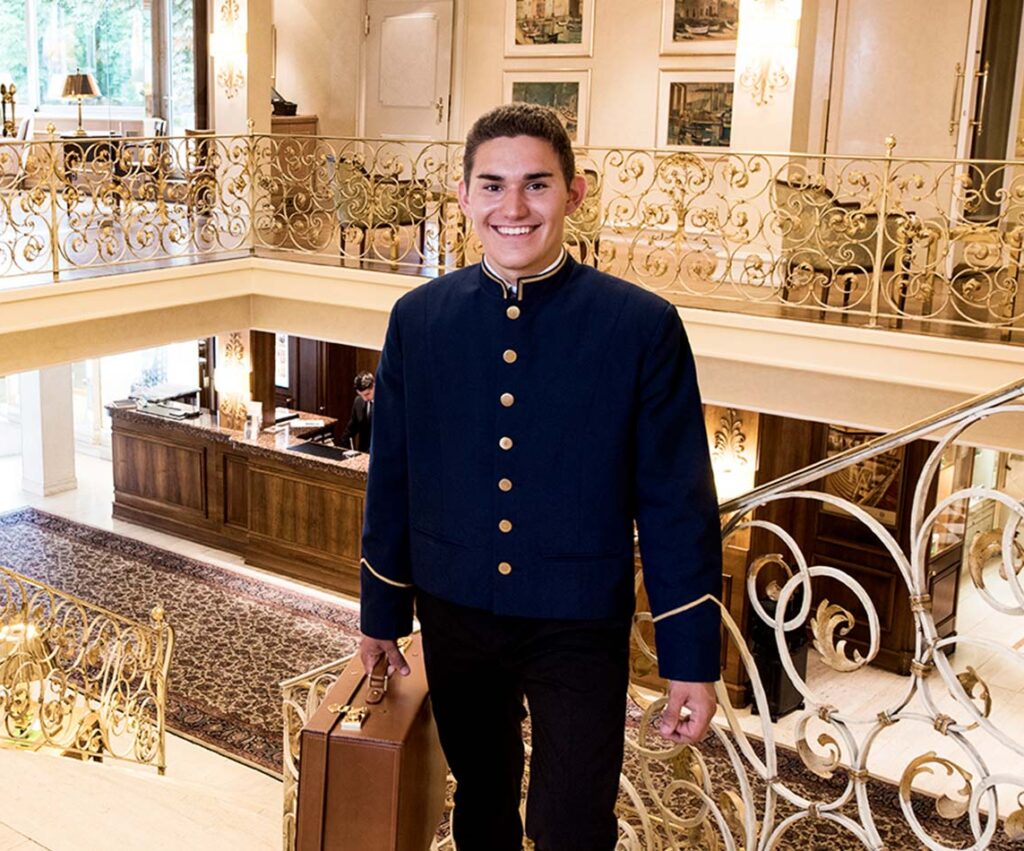 Luxushotel-Lobby: lächelnder Portier mit Koffer – professioneller Empfang, Concierge- & Gepäckservice.